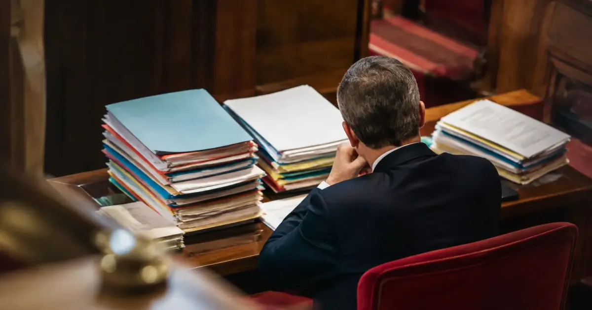 Député assis seul devant des dossiers budgétaires empilés