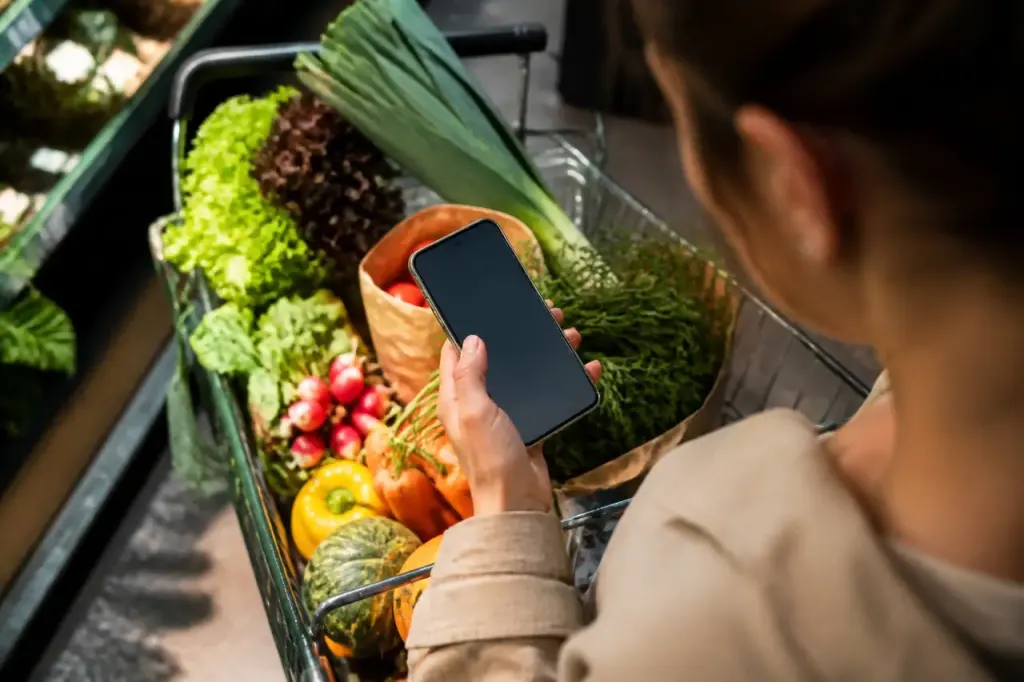 Smartphone sur un caddie rempli de legumes frais